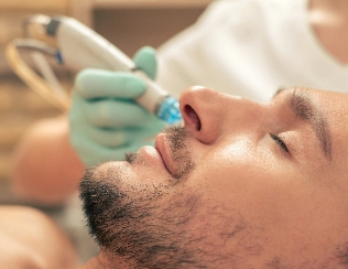 Man undergoing a facial treatment with a skincare device by a practitioner in light blue gloves, in a serene spa or clinic setting, emphasizing themes of self-care and grooming.